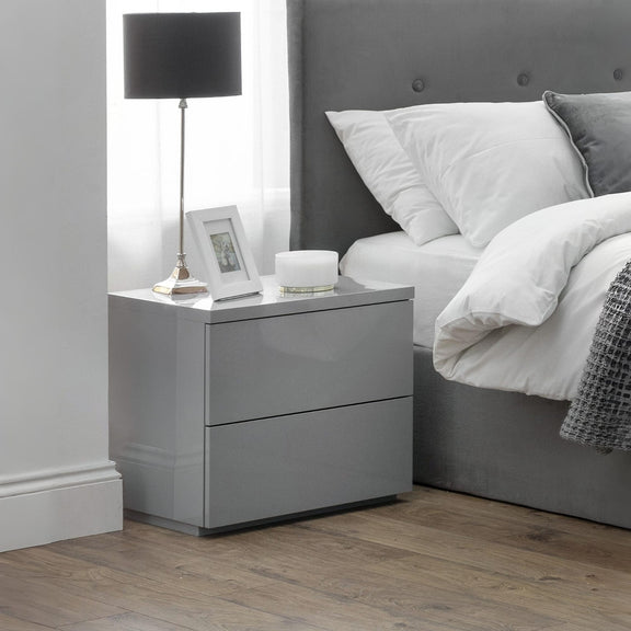Gray nightstand with a lamp and photo frame next to a bed with gray headboard and white bedding.