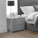 Gray nightstand with a lamp and photo frame next to a bed with gray headboard and white bedding.