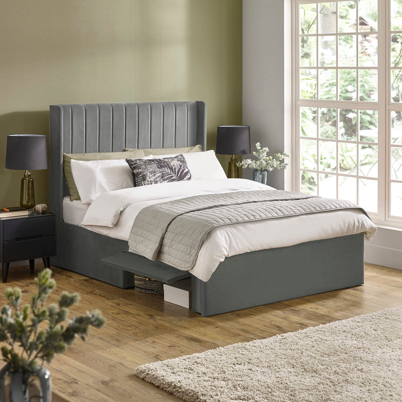 Gray upholstered bed in a bedroom with a large window and decorative elements.
