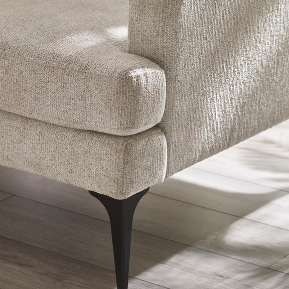 Close-up of a textured beige sofa with black legs on a wooden floor.