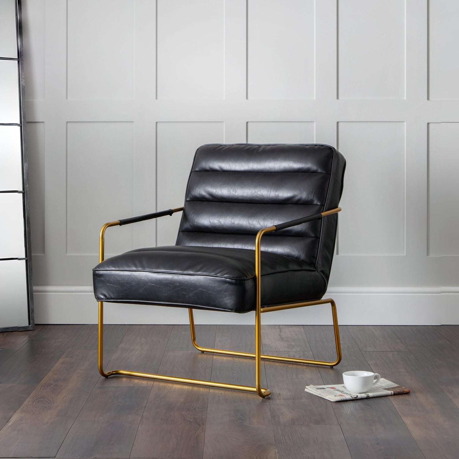Black leather armchair with gold frame on a wooden floor against a gray wall.