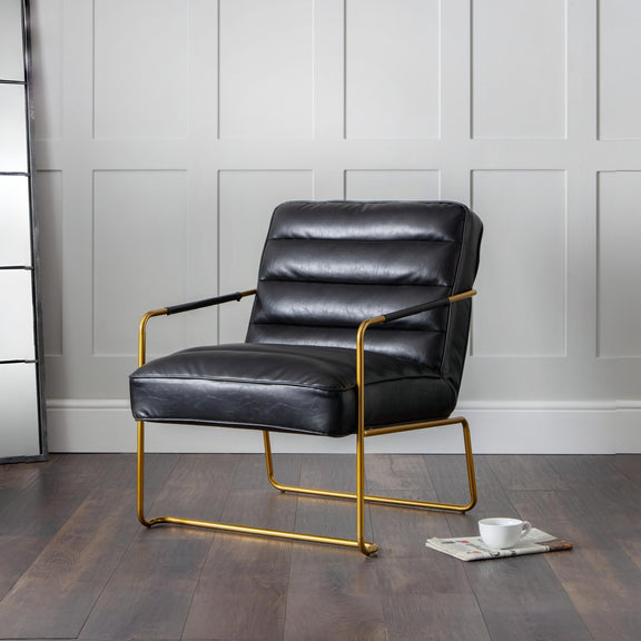 Black leather armchair with gold frame on a wooden floor against a gray wall.