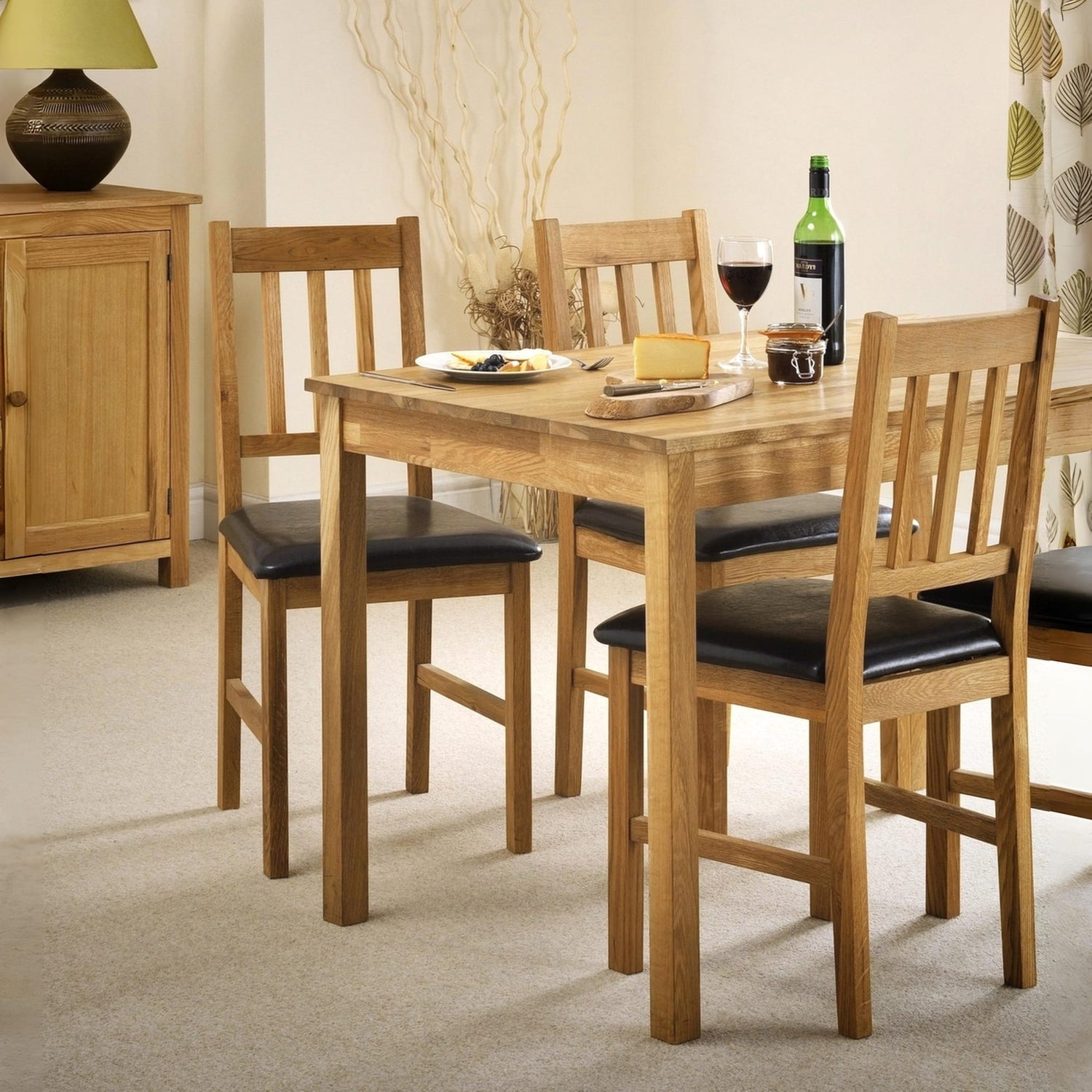 Wooden dining table with four chairs and a bottle of wine in a room setting.