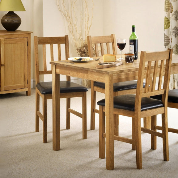 Wooden dining table with four chairs and a bottle of wine in a room setting.