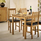 Wooden dining table with four chairs and a bottle of wine in a room setting.