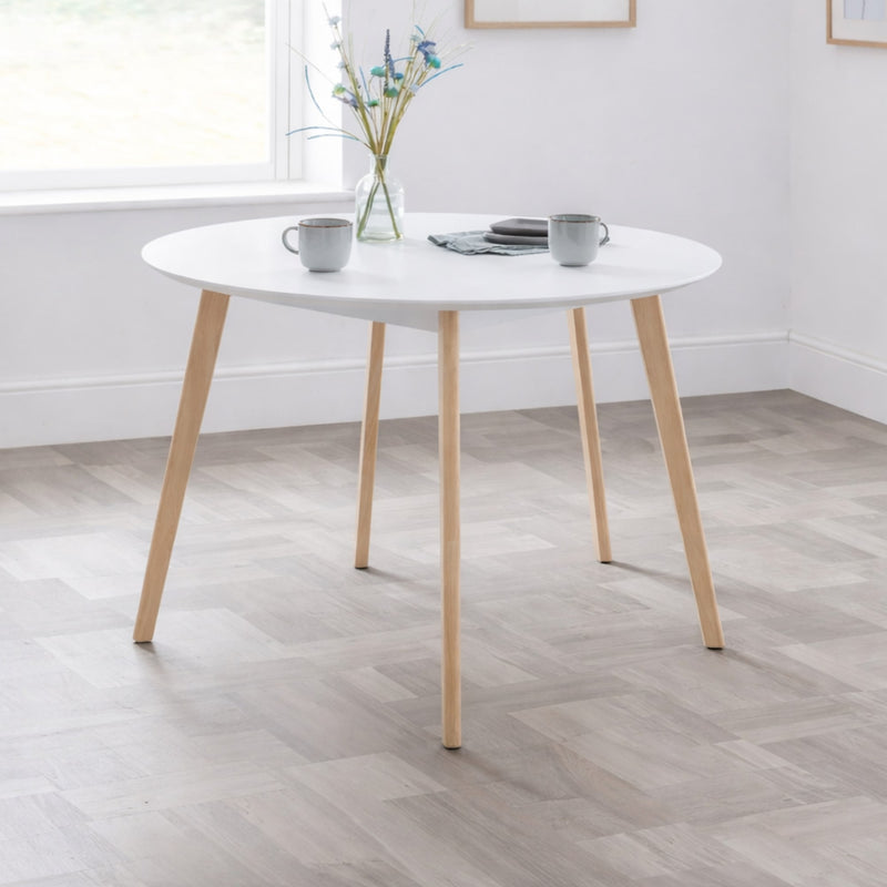 Round white table with wooden legs in a room with a window and light-colored floor.