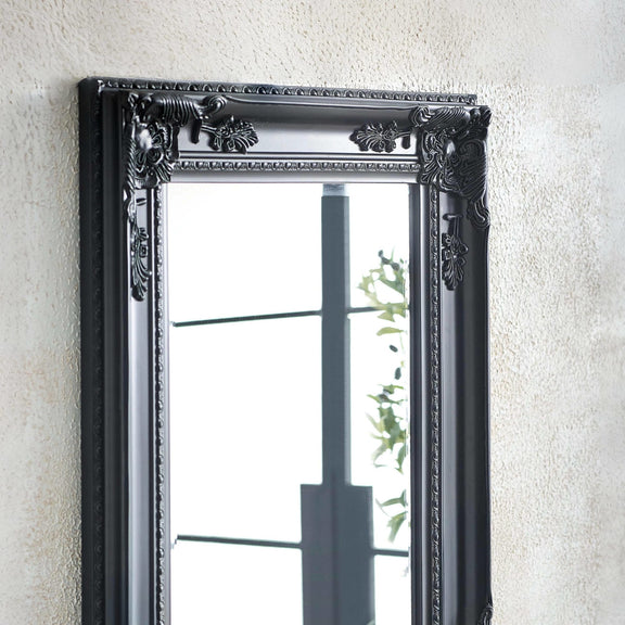 Decorative black mirror with intricate detailing on a textured wall.