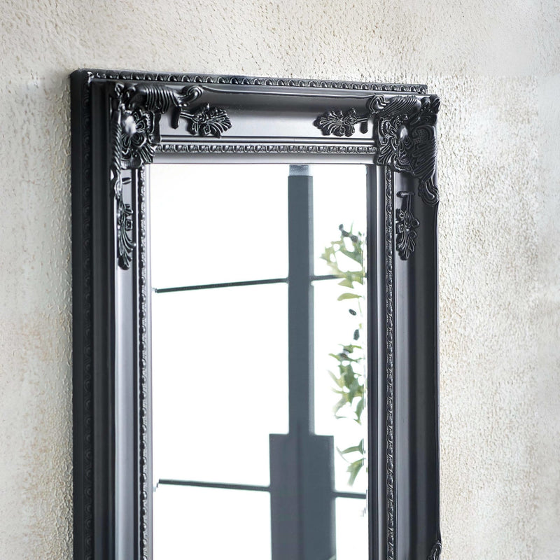 Decorative black mirror with intricate detailing on a textured wall.
