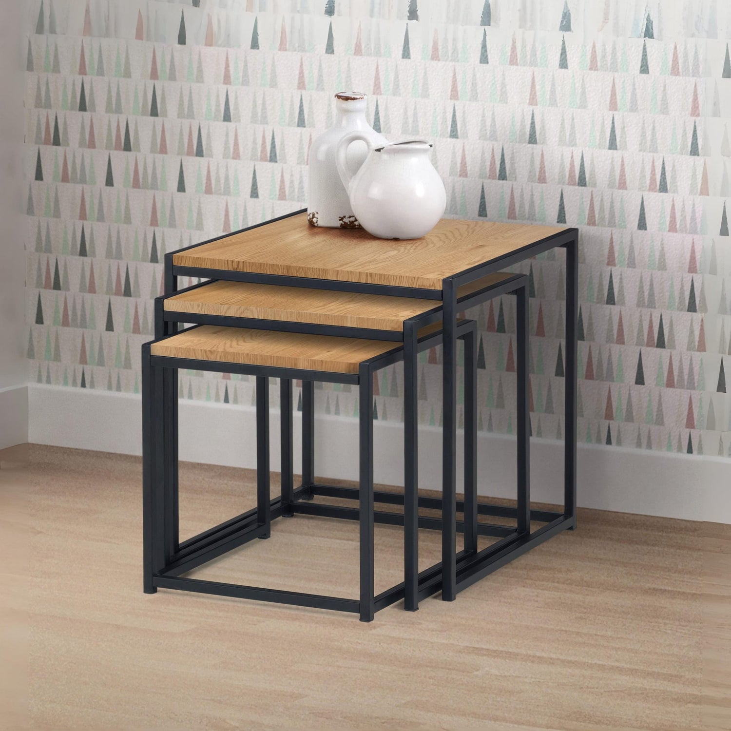 Set of three nesting tables with a white pitcher on top against a patterned wall.