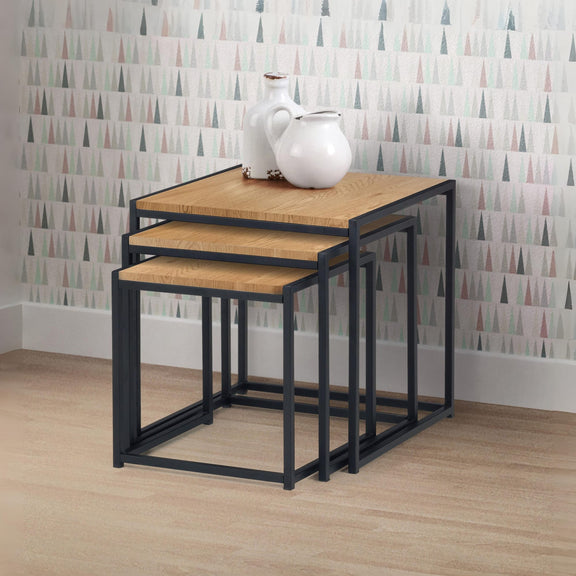 Set of three nesting tables with a white pitcher on top against a patterned wall.