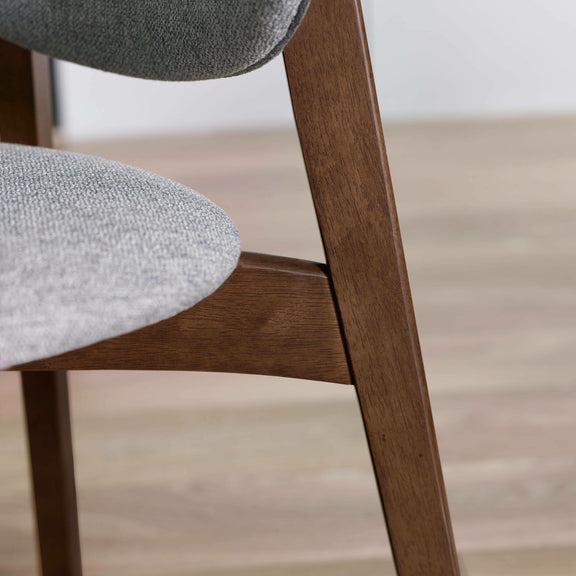 Close-up of a chair with wooden legs and gray cushioned seats on a light wood floor.