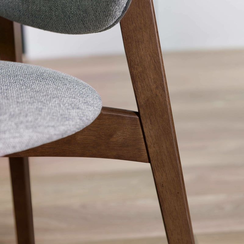 Close-up of a chair with wooden legs and gray cushioned seats on a light wood floor.