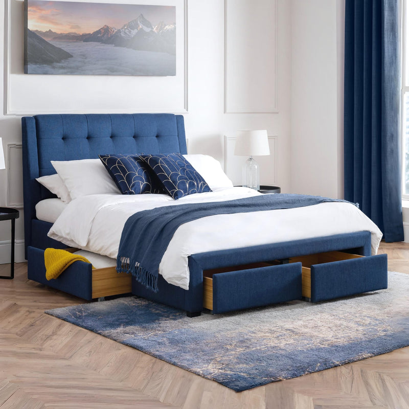 Blue upholstered bed with storage drawers in a bedroom setting.