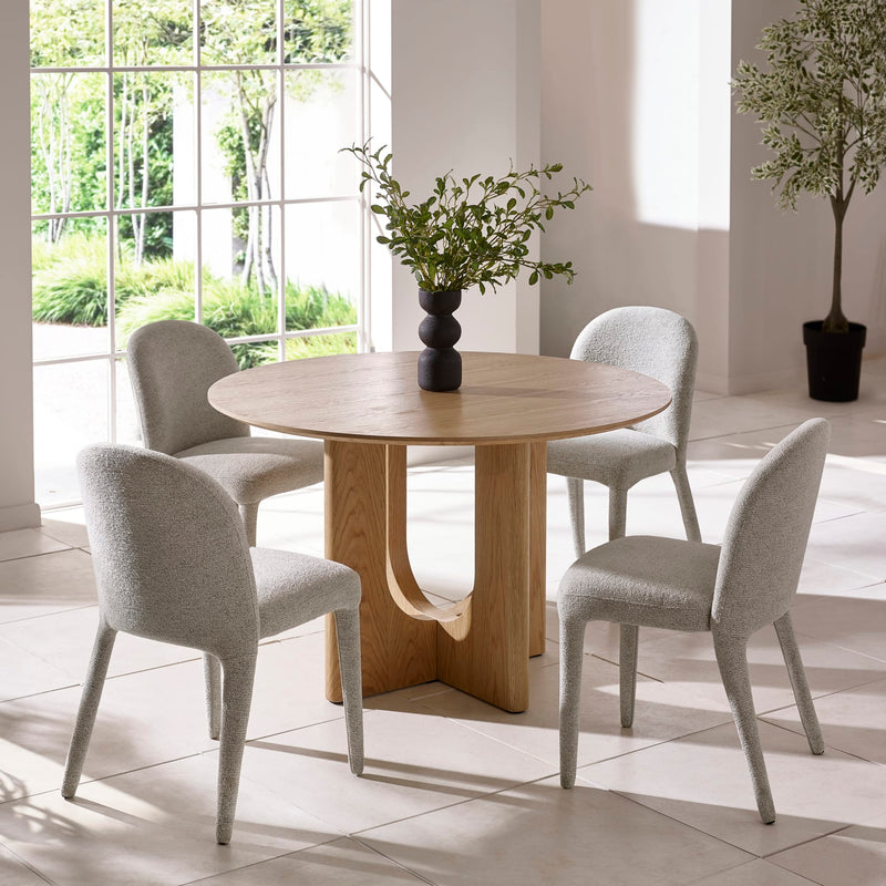 Dining room with a round wooden table and four gray chairs, featuring a vase with greenery on the table.