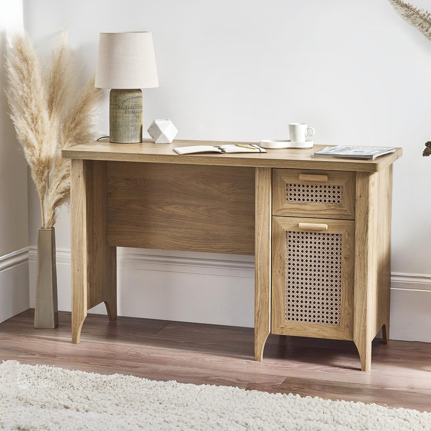 Wooden desk with a lamp, mug, and decorative items in a room setting.