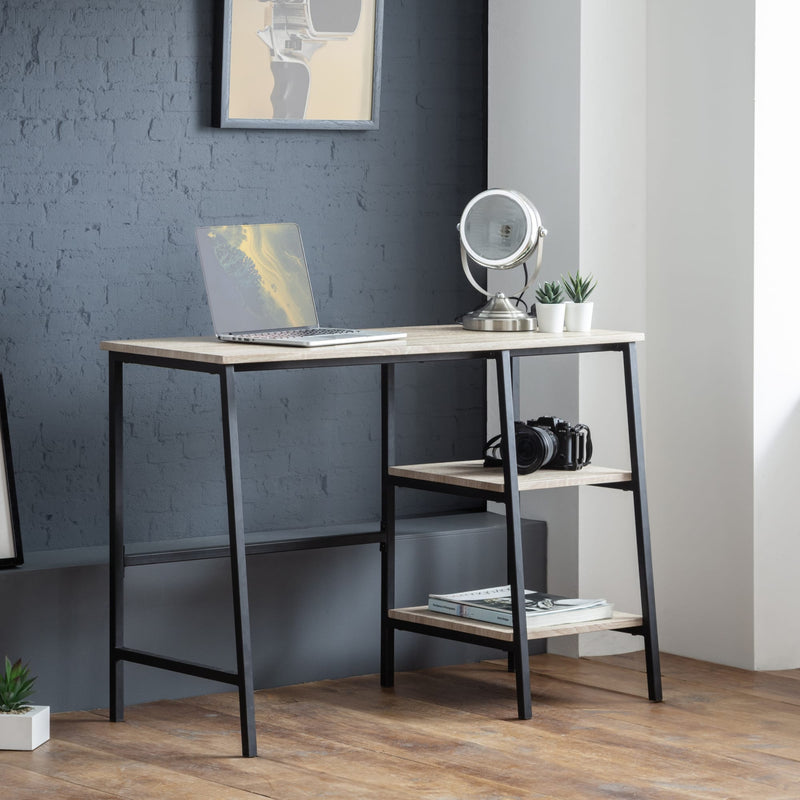 Modern desk with laptop, camera, and decorative items against a gray wall.