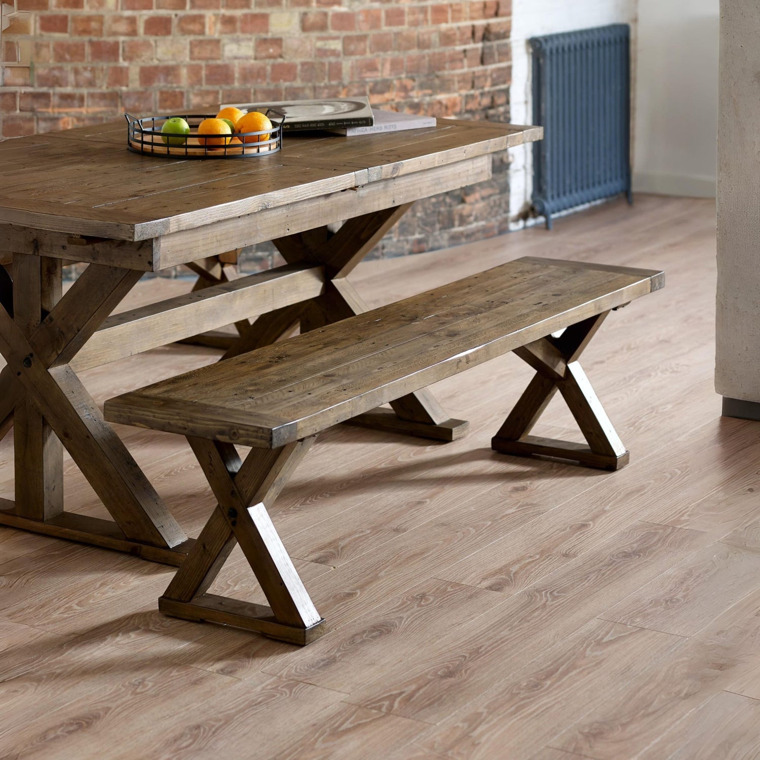 Wooden dining table with bench against a brick wall.