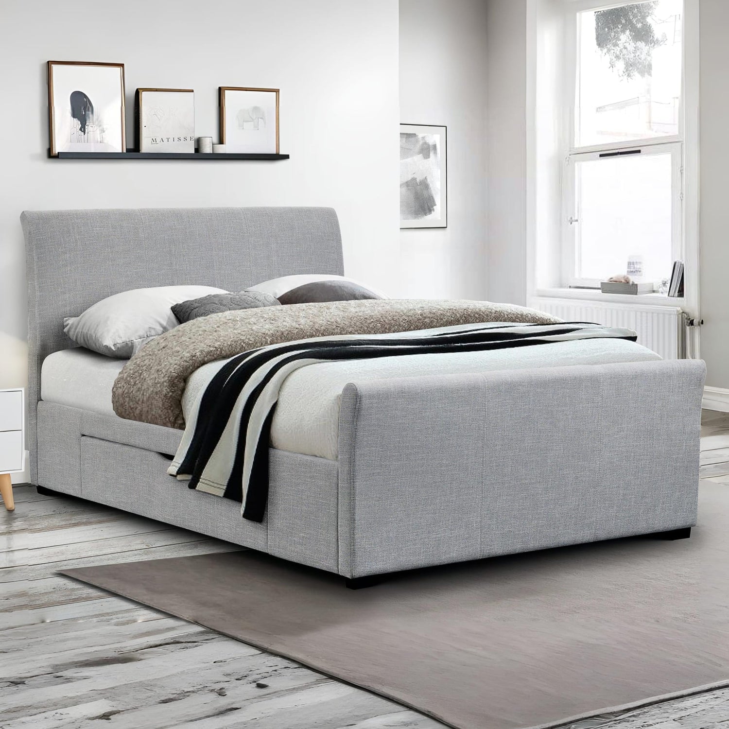 Gray upholstered bed in a room with framed pictures on the wall.