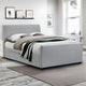 Gray upholstered bed in a room with framed pictures on the wall.