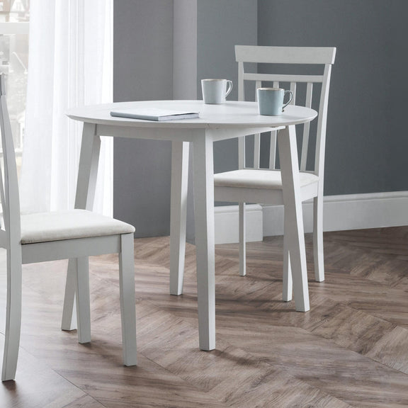 White dining table with chairs in a room with gray walls and wooden flooring.