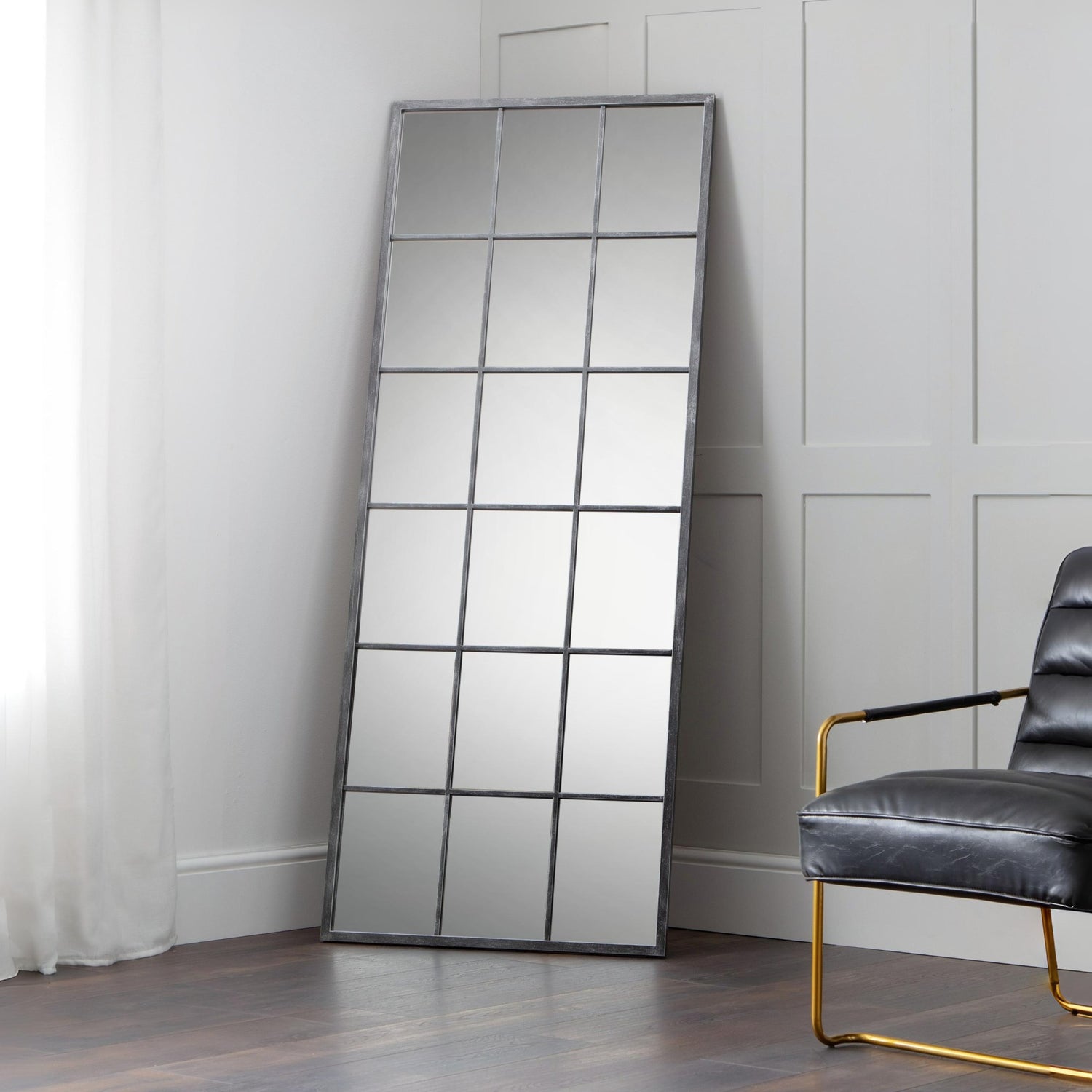 Tall floor mirror with grid design in a room with a chair and white walls.
