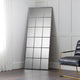 Tall floor mirror with grid design in a room with a chair and white walls.