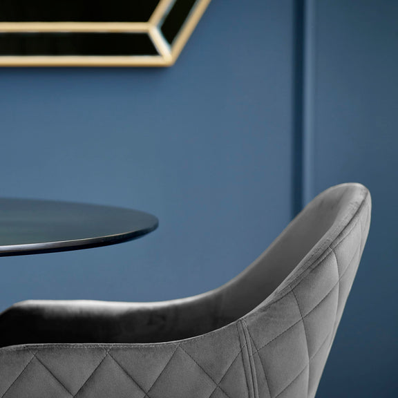 Gray quilted chair against a blue wall with a small round table.