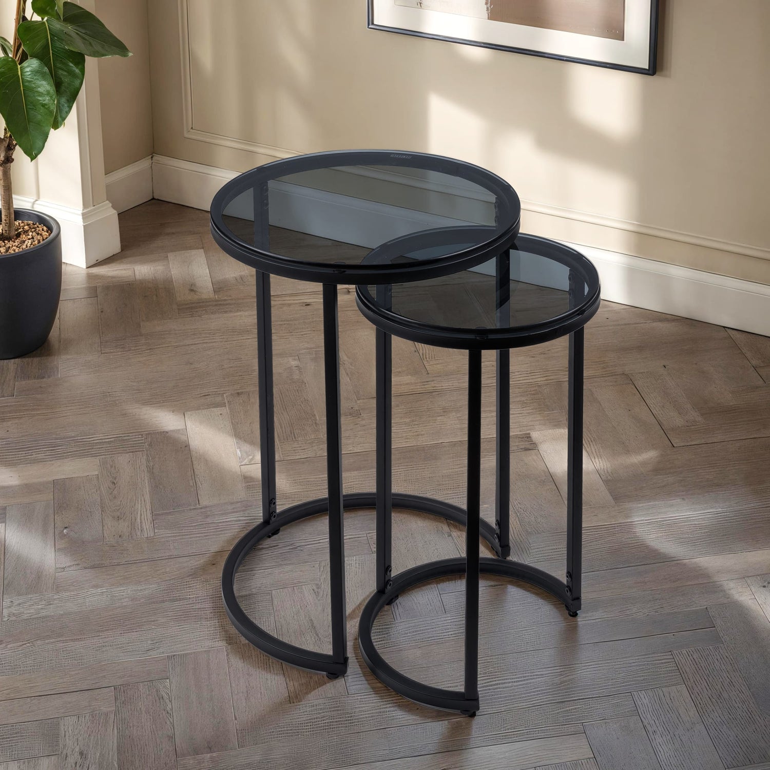 Set of two black nesting tables on a wooden floor with a plant in the background.