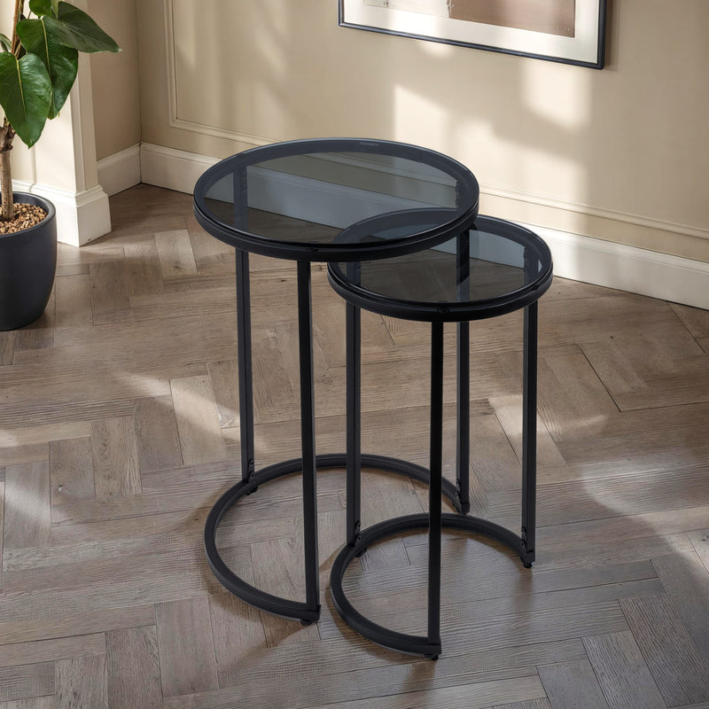 Set of two black nesting tables on a wooden floor with a plant in the background.