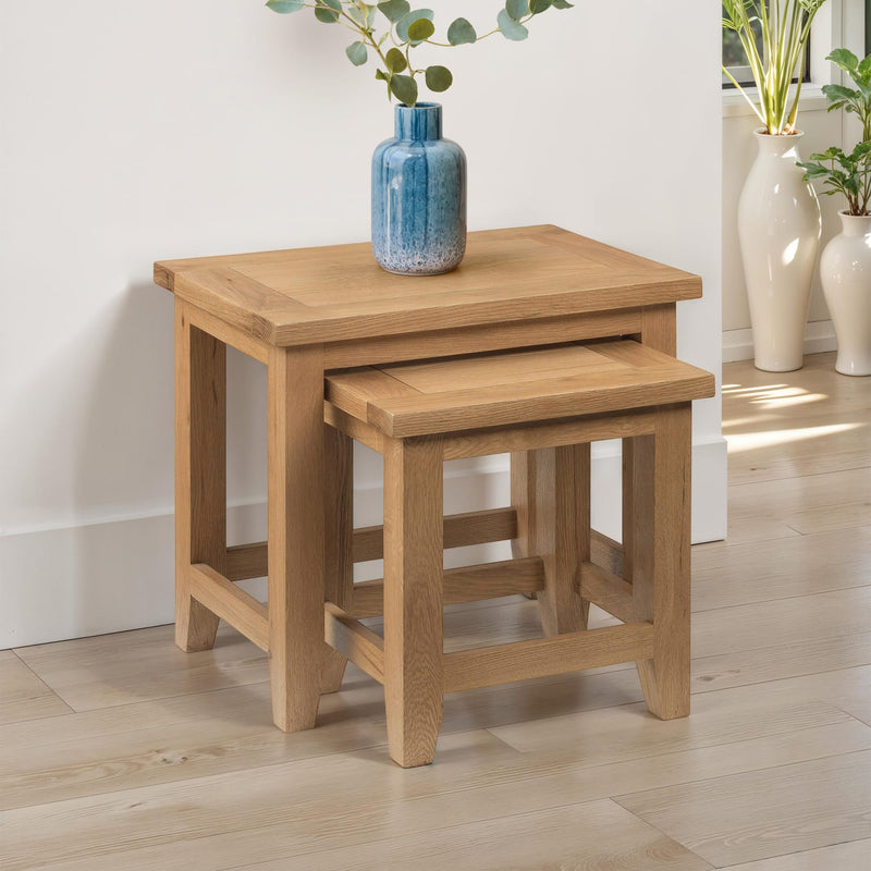 Two wooden nesting tables with a blue vase on top in a room setting.
