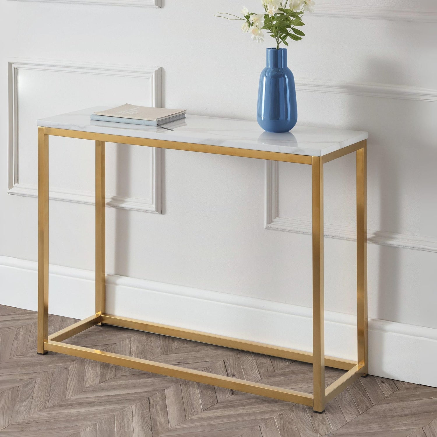 Console table with gold frame and marble top, featuring a blue vase and books against a white wall.