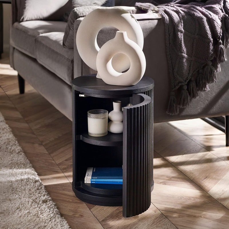 Black side table with decorative items next to a gray sofa on a wooden floor.