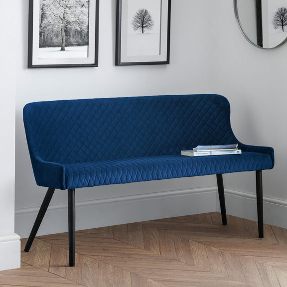 Blue quilted bench in a room with framed pictures on the wall.