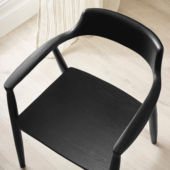 Black chair on a light wooden floor with a white curtain in the background
