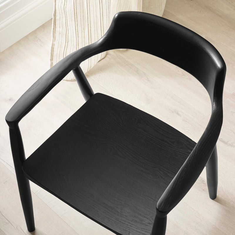Black chair on a light wooden floor with a white curtain in the background