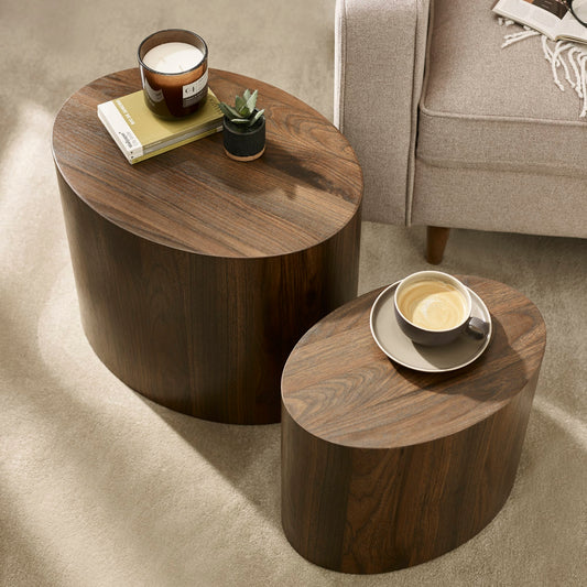 Two wooden side tables with a candle and a cup on a carpeted floor.