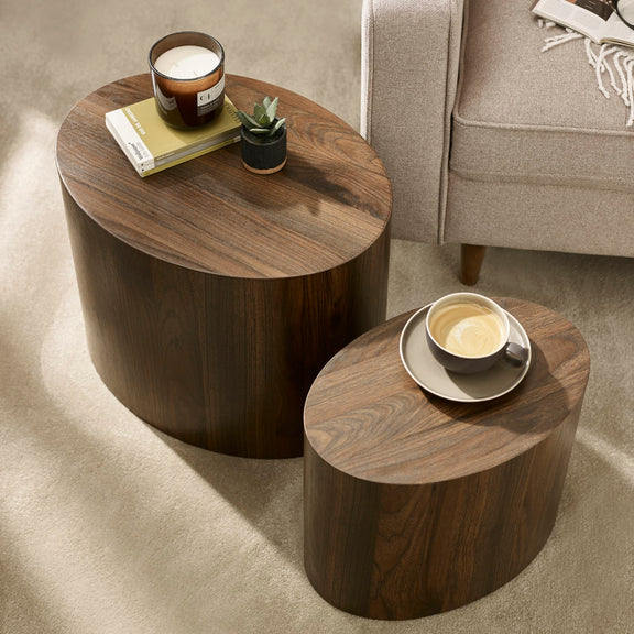 Two wooden side tables with a candle and a cup on a carpeted floor.