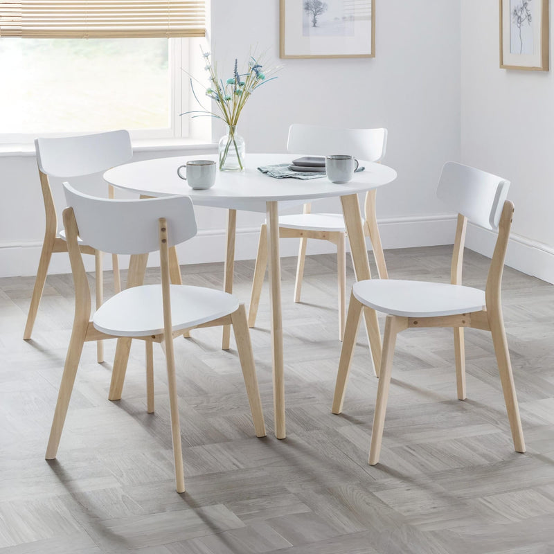Round white table with four matching chairs in a bright room.