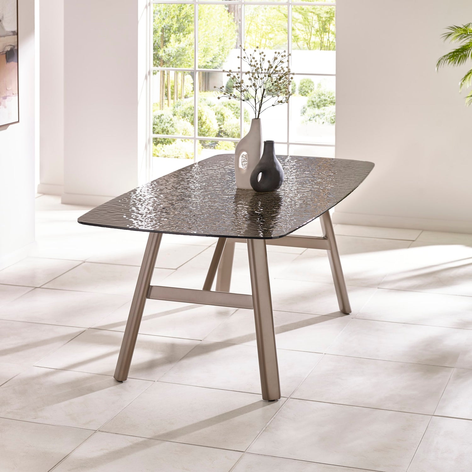 Dining table with a textured surface in a bright room with large windows.