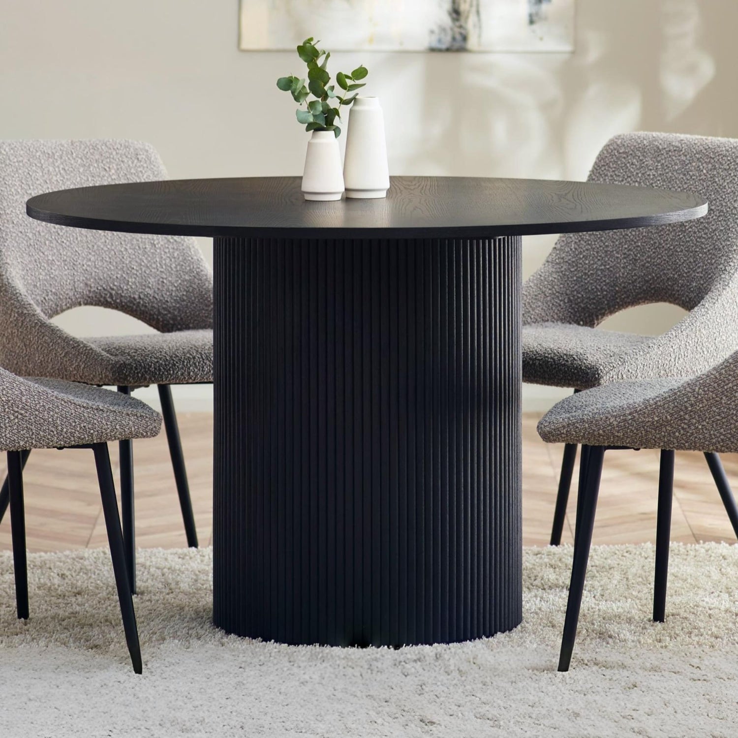 Black round dining table with textured cylindrical base in a room setting.