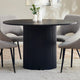 Black round dining table with textured cylindrical base in a room setting.