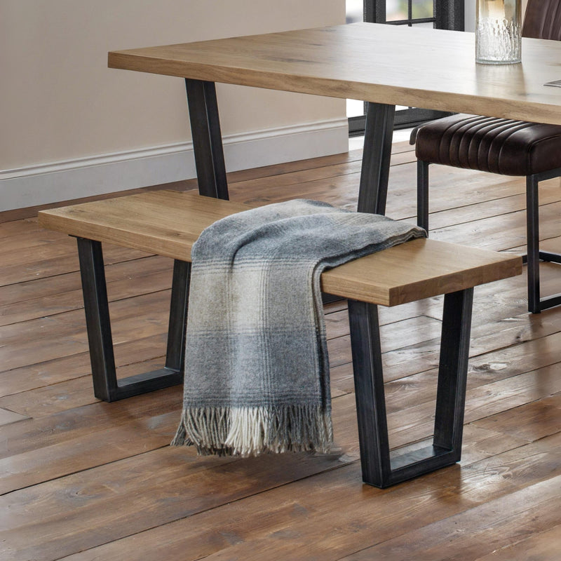 Wooden bench with a plaid blanket draped over it in a room with a wooden floor.