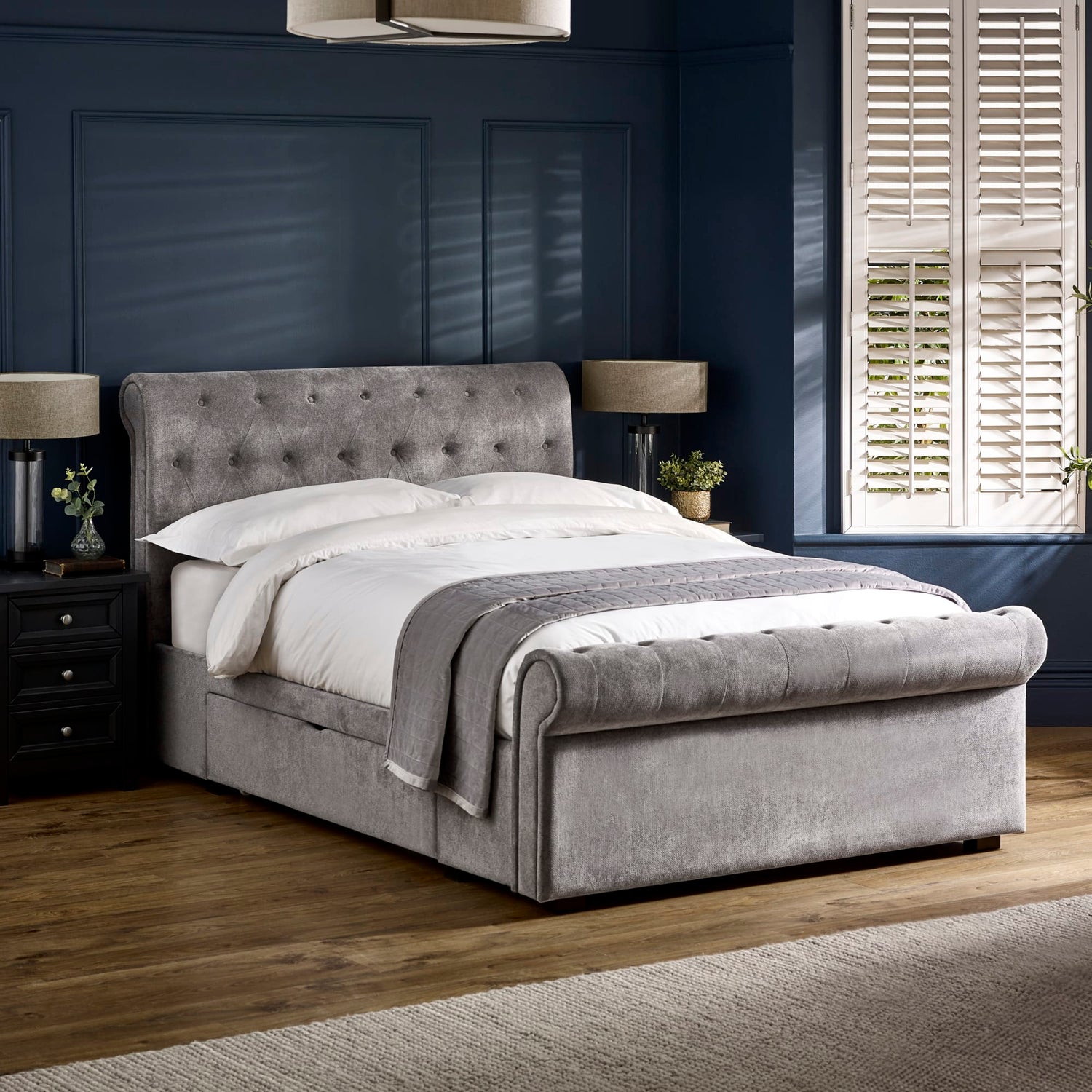 Gray upholstered bed in a bedroom with dark walls and a window.