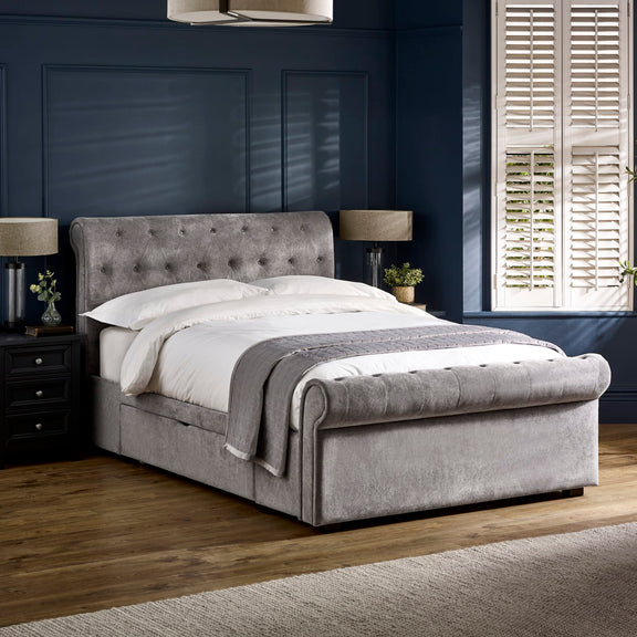 Gray upholstered bed in a bedroom with dark walls and a window.