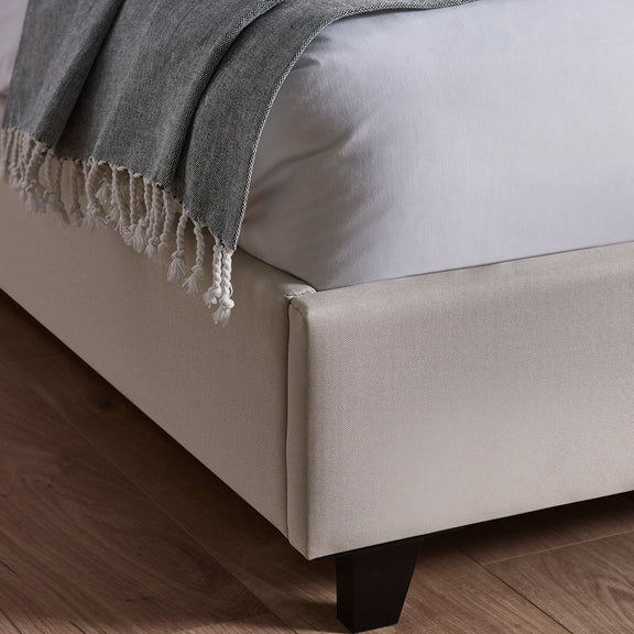 Gray blanket draped over a beige bed with wooden floor