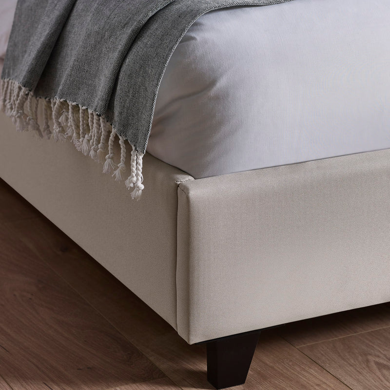 Gray blanket draped over a beige bed with wooden floor