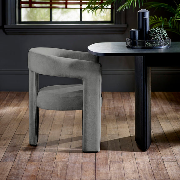 Gray chair next to a black dining table with decorative items in a room with wooden flooring and a window.