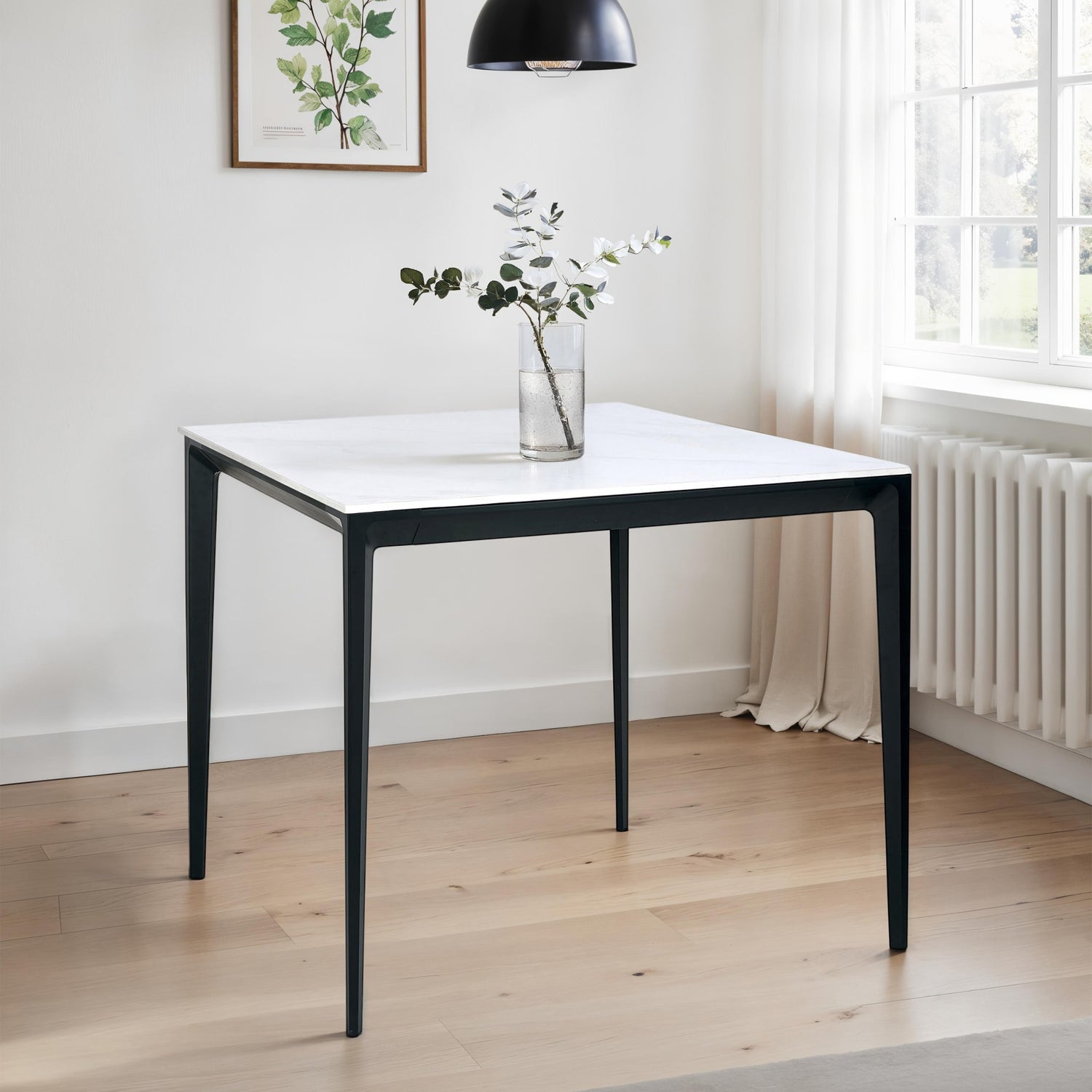 Square table with a white top and black legs in a room with a radiator and window.