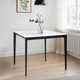 Square table with a white top and black legs in a room with a radiator and window.