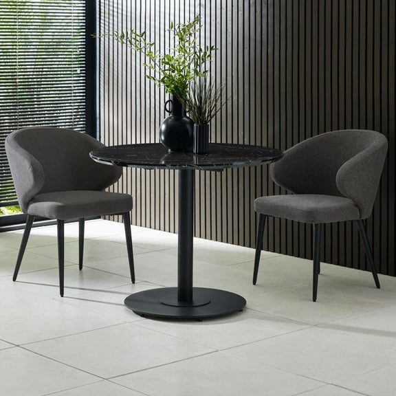 Two gray chairs around a black round table with a vase of plants in a modern setting.